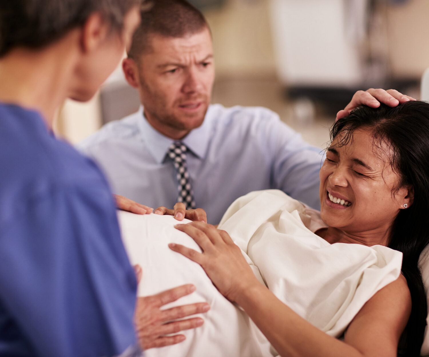 Shot of a young woman giving birth with her husband supporting her in the background.